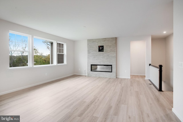 unfurnished living room featuring light wood-type flooring, a fireplace, baseboards, and recessed lighting