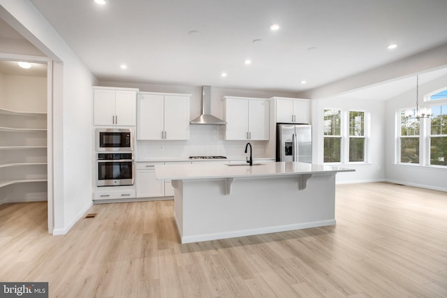 kitchen with stainless steel appliances, a sink, white cabinetry, wall chimney exhaust hood, and an island with sink