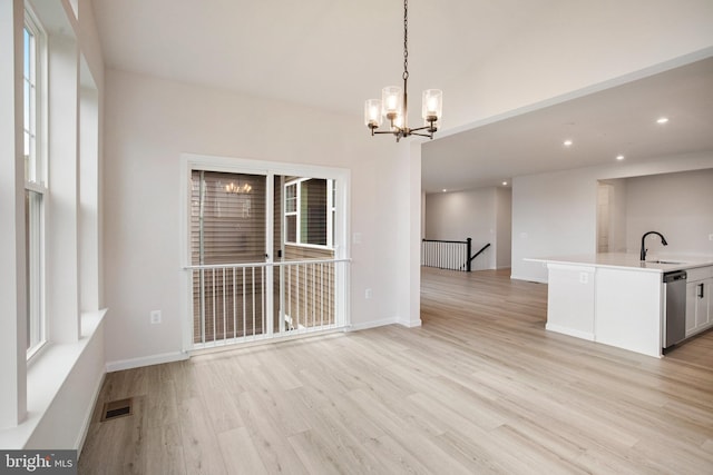 unfurnished dining area featuring visible vents, baseboards, a sink, light wood-style floors, and a notable chandelier