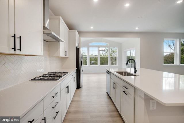 kitchen featuring light countertops, backsplash, appliances with stainless steel finishes, a sink, and wall chimney range hood