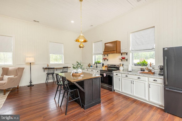 kitchen with dark wood-type flooring, electric stove, custom range hood, black fridge, and a breakfast bar area