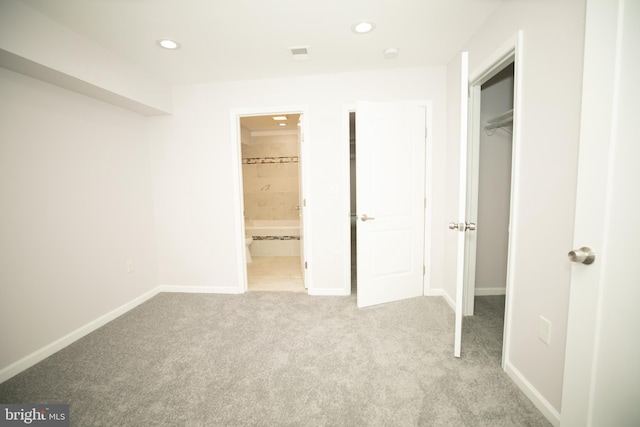 unfurnished bedroom featuring light carpet, ensuite bath, and a closet