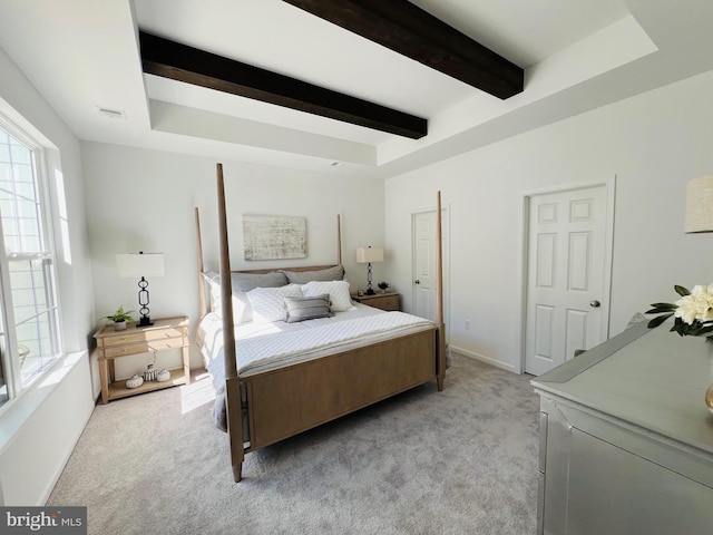 bedroom featuring beam ceiling, light carpet, and a tray ceiling