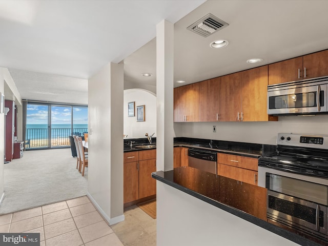 kitchen featuring light tile floors, dark stone counters, expansive windows, appliances with stainless steel finishes, and a water view