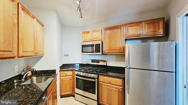 kitchen featuring appliances with stainless steel finishes, sink, light tile floors, dark stone countertops, and rail lighting