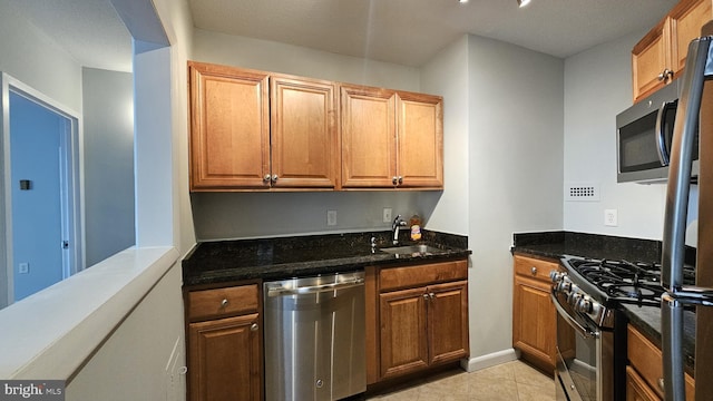 kitchen featuring appliances with stainless steel finishes, sink, dark stone counters, and light tile flooring