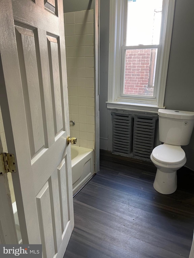 bathroom with wood-type flooring, tiled shower / bath, and toilet