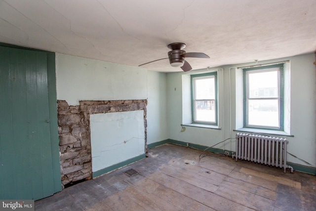 unfurnished room featuring radiator heating unit, ceiling fan, a fireplace, and hardwood / wood-style flooring