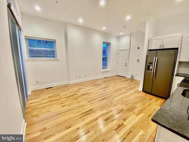 kitchen with dark stone counters, light wood-type flooring, white cabinetry, and stainless steel refrigerator with ice dispenser