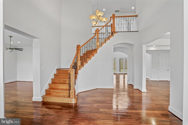 staircase featuring a towering ceiling, ceiling fan with notable chandelier, and wood-type flooring