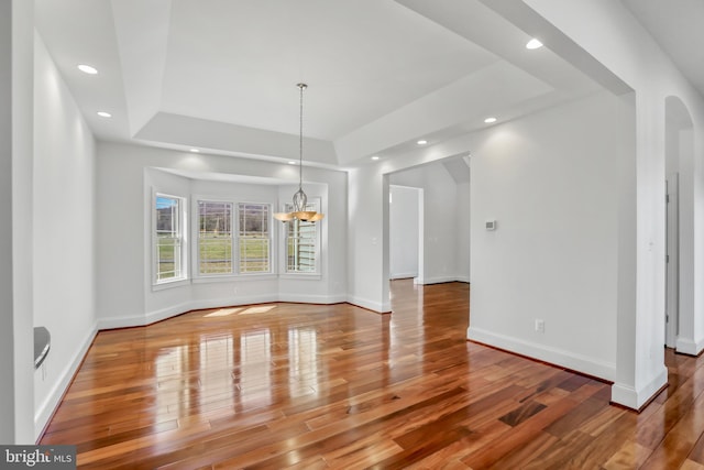 empty room featuring a notable chandelier, a tray ceiling, and wood-type flooring