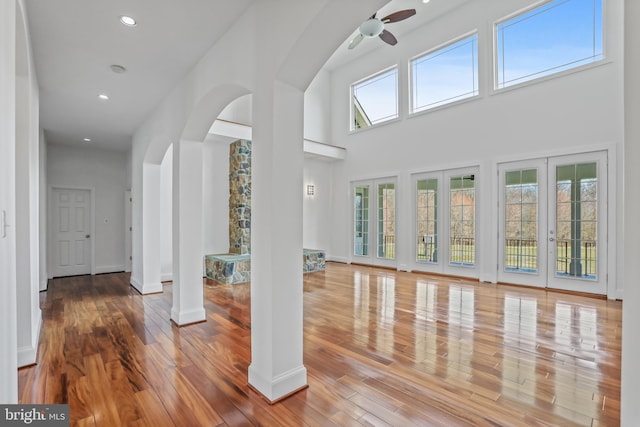 interior space with a towering ceiling, ceiling fan, light hardwood / wood-style floors, and french doors