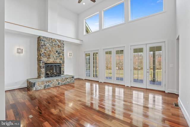 unfurnished living room featuring a stone fireplace, ceiling fan, a wealth of natural light, and a towering ceiling