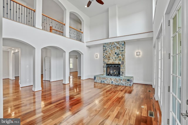 unfurnished living room with a towering ceiling, a fireplace, ceiling fan, and wood-type flooring