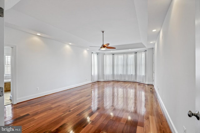 unfurnished room with ceiling fan, a raised ceiling, and wood-type flooring