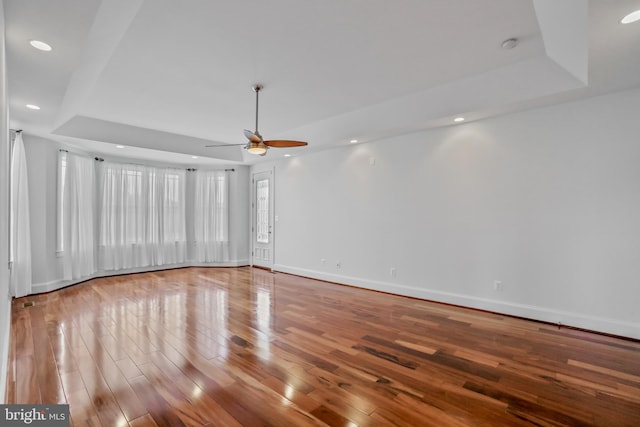 empty room with ceiling fan, a tray ceiling, and hardwood / wood-style flooring