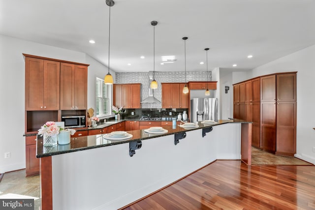 kitchen featuring light hardwood / wood-style floors, decorative light fixtures, stainless steel appliances, and a kitchen island with sink