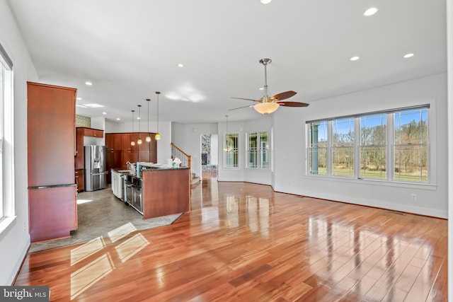 kitchen with a center island with sink, ceiling fan, stainless steel fridge, and light wood-type flooring