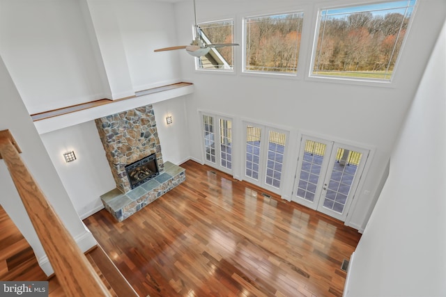 living room with a stone fireplace, ceiling fan, a towering ceiling, and a healthy amount of sunlight