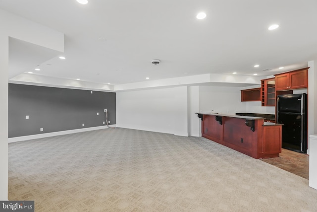 kitchen with black refrigerator, a kitchen bar, a kitchen island, and light colored carpet