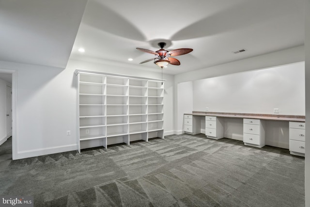 unfurnished office with dark carpet, ceiling fan, and built in desk