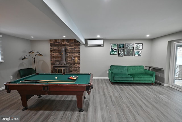 recreation room with billiards, light hardwood / wood-style flooring, a wood stove, and an AC wall unit