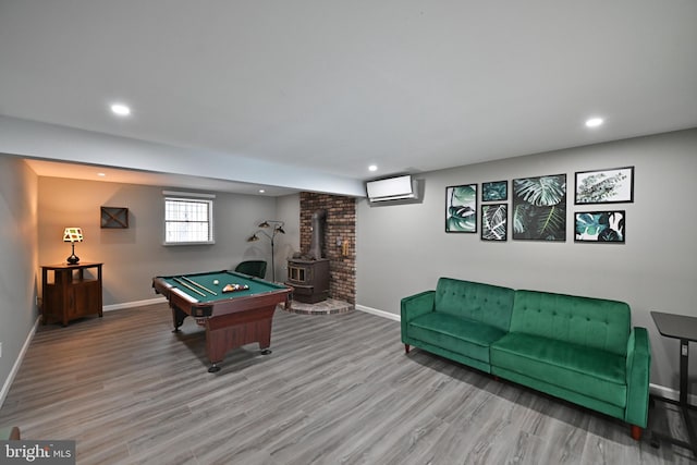 rec room featuring billiards, a wood stove, an AC wall unit, and light hardwood / wood-style floors