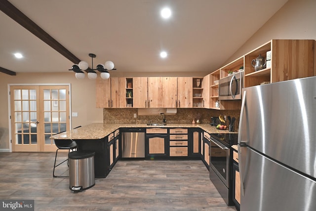 kitchen with kitchen peninsula, dark wood-type flooring, light stone countertops, appliances with stainless steel finishes, and a breakfast bar area