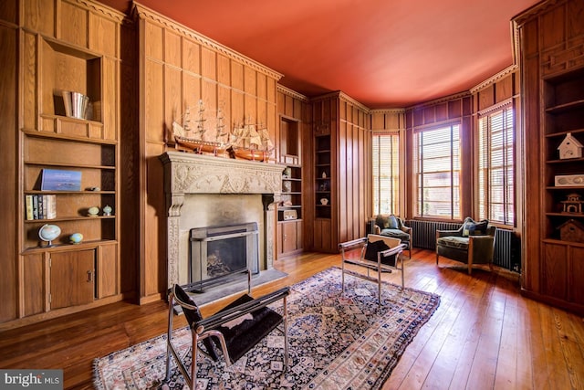 living room featuring built in features, wooden walls, dark hardwood / wood-style floors, and radiator