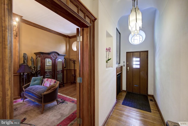 entryway featuring an inviting chandelier, crown molding, a towering ceiling, and light hardwood / wood-style flooring