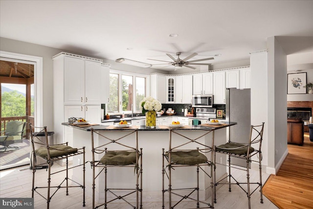 kitchen with backsplash, ceiling fan, light wood-type flooring, white cabinets, and appliances with stainless steel finishes