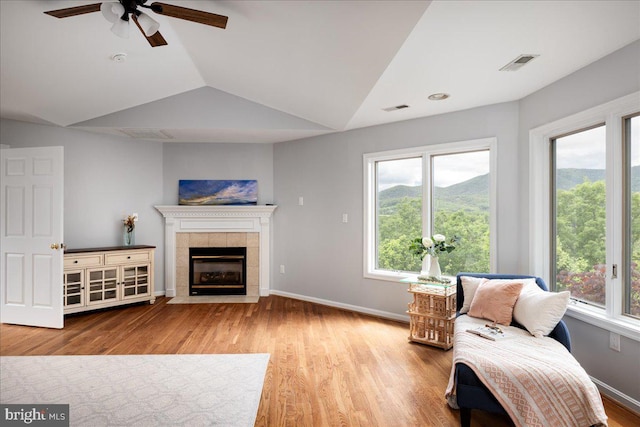 living room with ceiling fan, a tiled fireplace, hardwood / wood-style flooring, and lofted ceiling