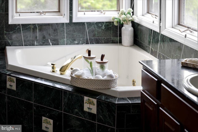 bathroom featuring tiled tub and vanity