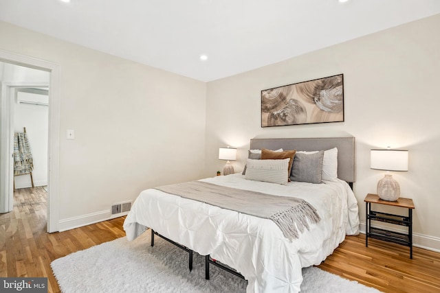 bedroom with hardwood / wood-style floors and a wall mounted AC