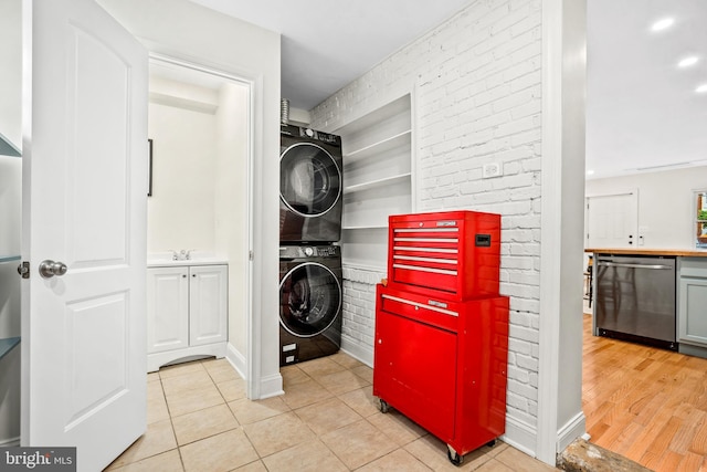 laundry room featuring light hardwood / wood-style floors, stacked washer / drying machine, and brick wall