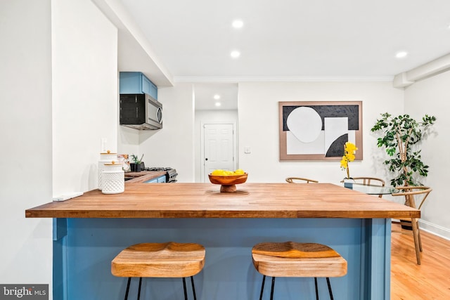 kitchen with light wood-type flooring, blue cabinets, a breakfast bar area, and kitchen peninsula