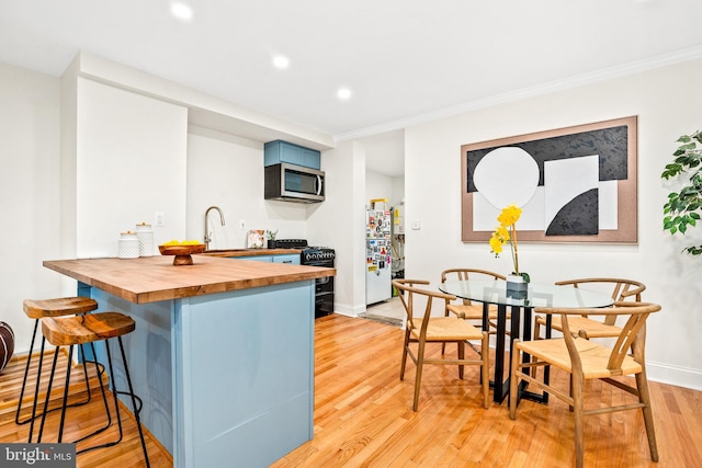 kitchen with butcher block countertops, blue cabinetry, a kitchen bar, light hardwood / wood-style flooring, and black range