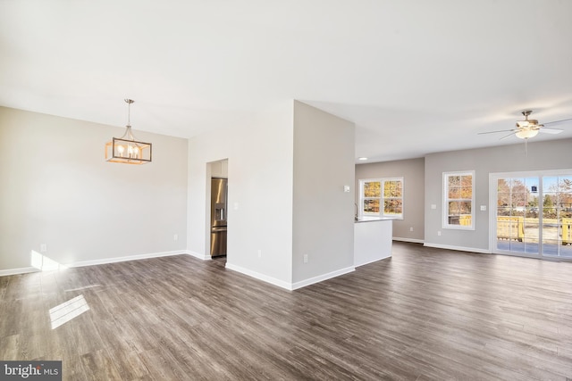 unfurnished living room featuring ceiling fan with notable chandelier and dark hardwood / wood-style flooring