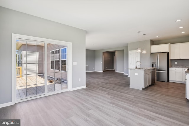 kitchen with stainless steel appliances, white cabinetry, pendant lighting, light stone countertops, and a kitchen island with sink