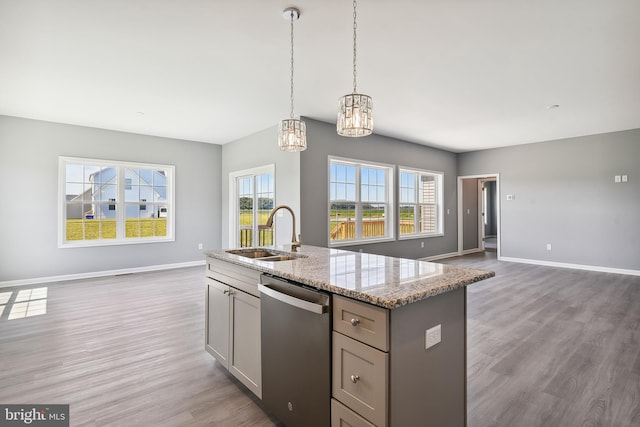 kitchen featuring light stone countertops, dishwasher, an island with sink, an inviting chandelier, and sink