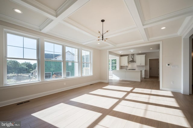 unfurnished living room with an inviting chandelier, light wood-type flooring, beam ceiling, coffered ceiling, and crown molding