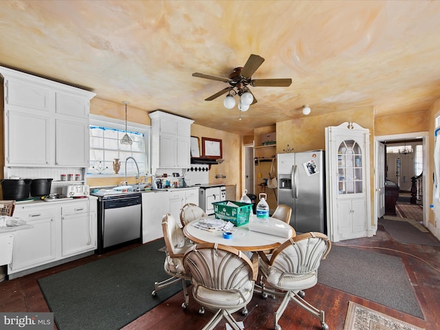 kitchen featuring pendant lighting, appliances with stainless steel finishes, dark wood-type flooring, ceiling fan with notable chandelier, and white cabinetry