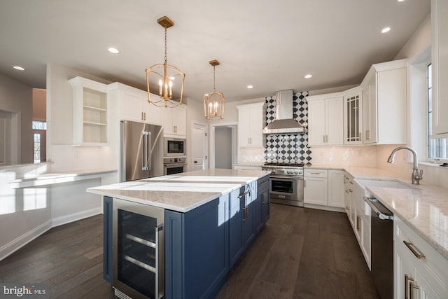 kitchen featuring wall chimney exhaust hood, high end appliances, beverage cooler, blue cabinetry, and tasteful backsplash