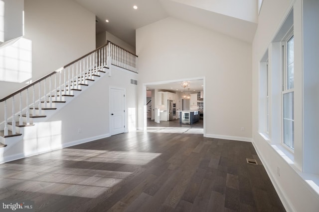 unfurnished living room with dark hardwood / wood-style flooring, high vaulted ceiling, an inviting chandelier, and a healthy amount of sunlight