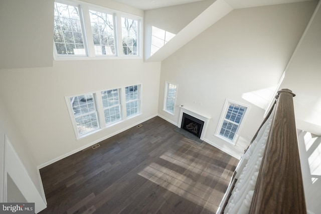 unfurnished living room with high vaulted ceiling and dark wood-type flooring