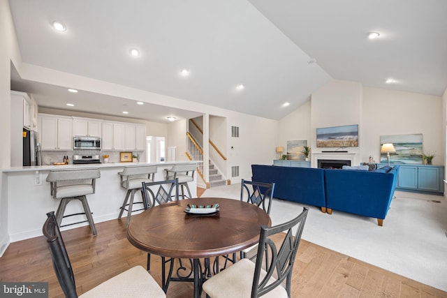 dining area featuring high vaulted ceiling and light carpet