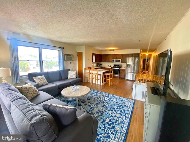 living room featuring a textured ceiling, light wood-type flooring, and a wall mounted air conditioner