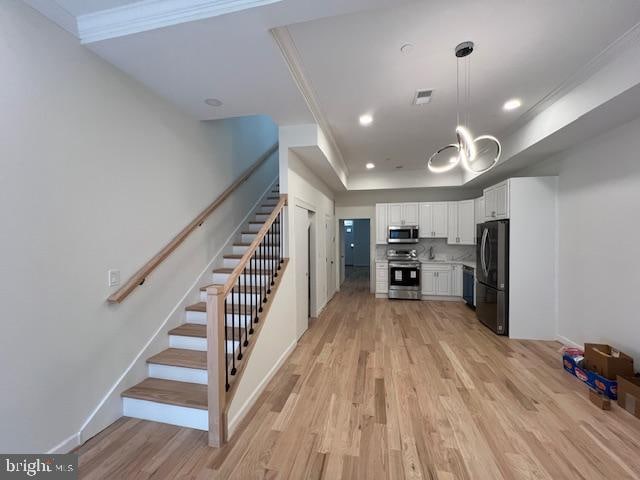 kitchen with white cabinets, hanging light fixtures, stainless steel appliances, light wood-type flooring, and crown molding