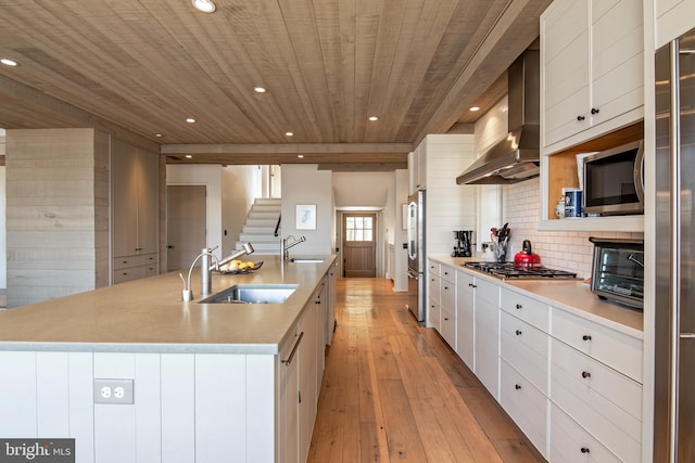 kitchen with white cabinetry, wall chimney range hood, sink, and an island with sink