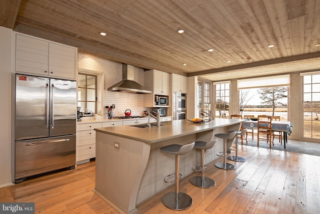 kitchen with white cabinets, wall chimney range hood, built in appliances, and light hardwood / wood-style floors